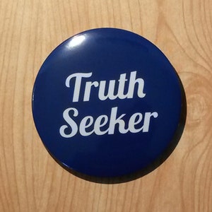 Può includere: Un bottone rotondo blu con testo bianco che dice "Truth Seeker".