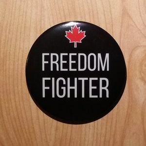 Może przedstawiać: Czarny guzik z czerwoną liściastą klonową i tekstem "FREEDOM FIGHTER" w kolorze białym.