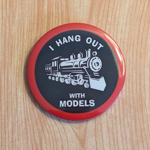 May include: A red and black button with a white train and the text "I hang out with models".