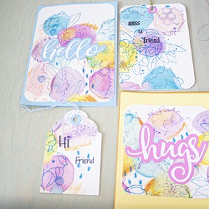 May include: Four handmade greeting cards with watercolor floral designs. The cards feature the words "hello", "miss you friend", "hi friend", and "hugs".