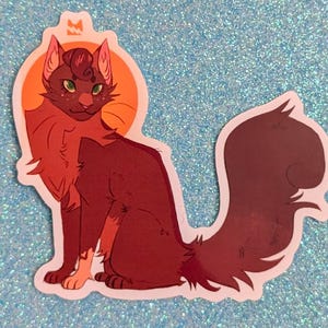 May include: A die-cut sticker featuring a stylized illustration of a dark reddish-brown cat with green eyes and a fluffy tail. The cat is sitting in front of a bright orange circular sun shape. The sticker has a white border and a smooth finish.