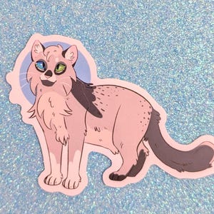 May include: A die-cut sticker featuring a stylized illustration of a cat with light pink fur, dark gray patches, and heterochromia, displaying one blue eye and one green eye. The cat is standing in profile against a circular light blue background.