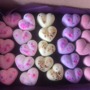 May include: A box of 24 heart-shaped wax melts in various colors, including pink, purple, white, and gold. The melts are arranged in a grid pattern and have a speckled or glittery finish.