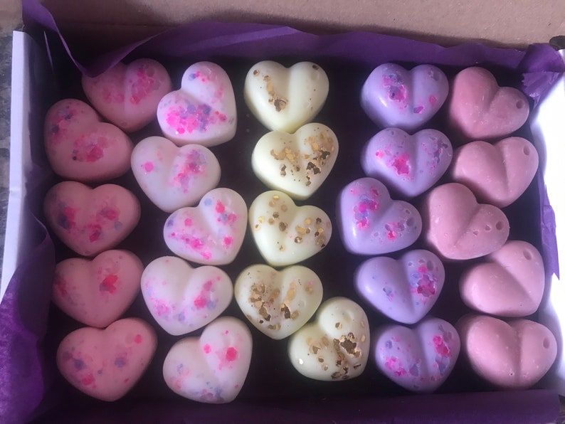 May include: A box of 24 heart-shaped wax melts in various colors, including pink, purple, white, and gold. The melts are arranged in a grid pattern and have a speckled or glittery finish.