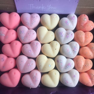 May include: A box filled with 27 heart-shaped wax melts in three colors: pink, yellow, and orange. Some of the melts have glitter on them.