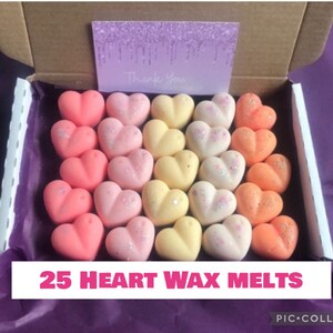 May include: A box filled with 25 heart-shaped wax melts in shades of pink, yellow, and orange. The melts are arranged in rows and have a glittery finish. The box is labeled "25 Heart Wax Melts".