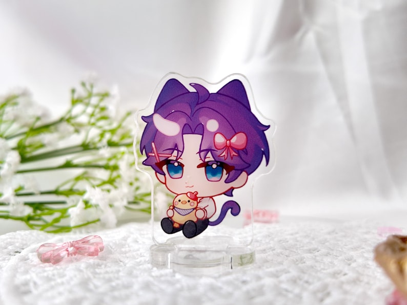 May include: A purple and white anime character with cat ears and a pink bow holding a yellow chick. The character is standing on a clear acrylic stand.