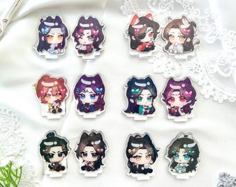 May include: A collection of acrylic anime character standees. Each standee features a chibi-style illustration of a character with detailed hair and clothing. The characters have various hair colors and are decorated with bows and other accessories. The standees are on a white surface.