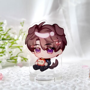 May include: A clear acrylic stand with a cartoon character holding an apple. The character has brown hair, purple eyes, and is wearing a black and white outfit. The character has dog ears and a pink bow in their hair.