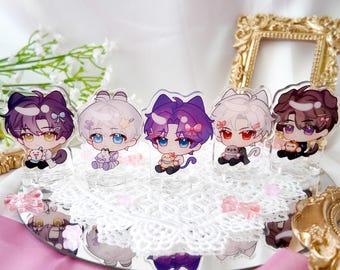 May include: Five colorful anime character acrylic stands with a white lace background. Each stand features a different character with a unique design and pose. The characters are holding small objects, such as a bunny or a flower.