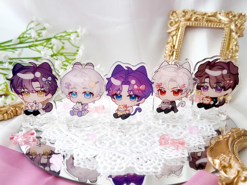 May include: Five colorful anime character acrylic stands with a white lace background. Each stand features a different character with a unique design and pose. The characters are holding small objects, such as a bunny or a flower.