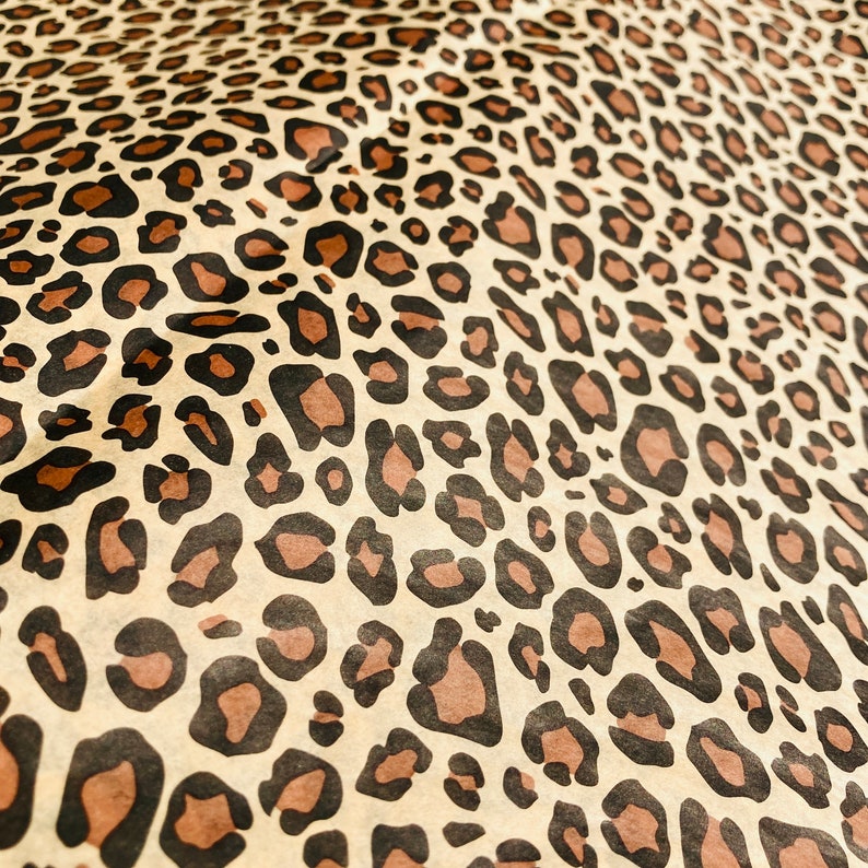 May include: A close-up of a brown and beige fabric with a leopard print pattern. The fabric has a textured surface and is made of a soft material.