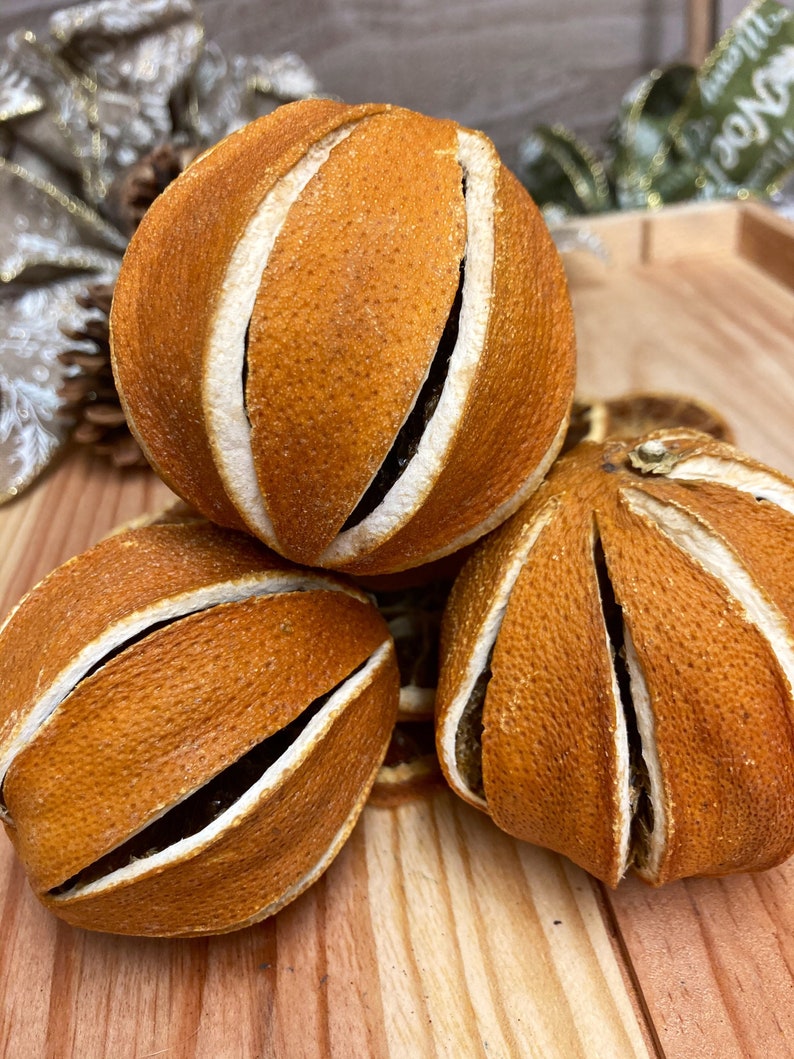 May include: Three dried orange slices, each with a unique pattern of cuts, are arranged on a wooden surface. The orange slices are a deep orange color and have a slightly textured surface.