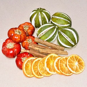 May include: An assortment of decorative items including dried orange slices, green and white striped orbs, red pepper-shaped ornaments, and cinnamon sticks. These items are arranged on a neutral surface, suggesting a fall or holiday theme.