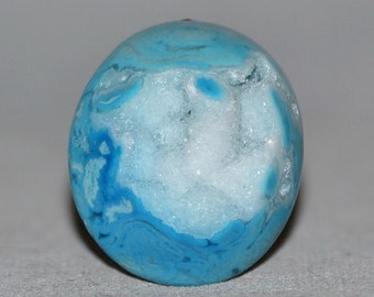 Op de afbeelding: Een ronde, blauwe en witte agaat edelsteen met een wit, kristallijn interieur.