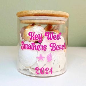 May include: A white ceramic mug with a black handle and the text "But First, Coffee" in a bold, black font. The mug is set against a blurred background, suggesting a cozy setting.