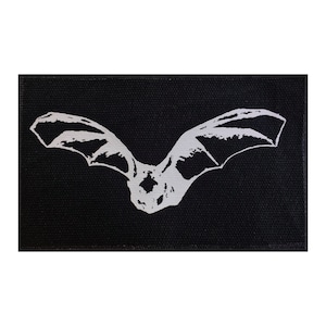 May include: A white silhouette of a bat on a black fabric background.