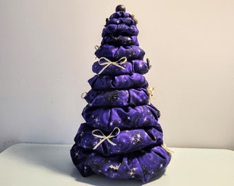 May include: A purple and gold fabric Christmas tree with a star-like pattern and white bows. The tree is made of multiple layers of fabric and is a unique and festive decoration.