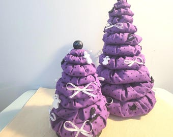 May include: Two purple fabric Halloween trees decorated with white ghosts, black spiders, and white bows. The trees are made of multiple layers of fabric and are stacked on top of each other to create a cone shape.