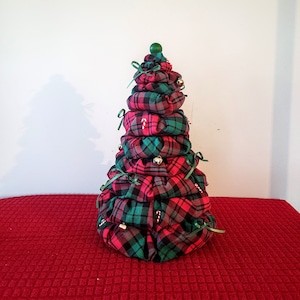 May include: A decorative Christmas tree made of red and green plaid fabric. The tree is tiered, with each tier tied with green ribbon. Small bells and candy canes are attached as ornaments. A green ball tops the tree.