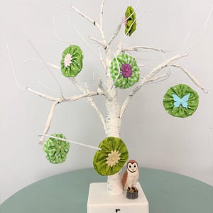 May include: A decorative white birch tree with green fabric ornaments and a small owl figurine. The ornaments are various shades of green with floral and butterfly accents. The owl is perched on a small wooden stump.