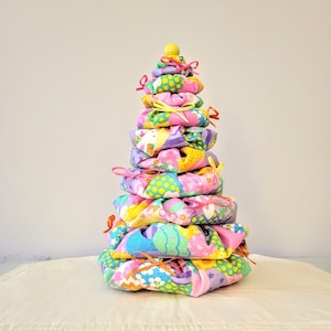 May include: A colorful fabric Christmas tree with a yellow star on top. The tree is made of multiple layers of fabric with different patterns, including pink, purple, yellow, and green.