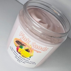 May include: A clear plastic jar of pink papaya mango body butter with a white label that reads "Pink Sands Papaya Mango Body Butter" and lists the ingredients: Shea Butter, Cocoa Butter, Mango Butter, Coconut Oil & Vitamin E Oil. The jar is 8 oz.