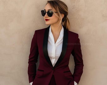 May include: A woman wearing a burgundy blazer with a black satin lapel and a white button-down shirt. She is wearing sunglasses and has her hair pulled back in a ponytail. The text "FASHION GENTLEMAN" is visible in the lower right corner of the image.