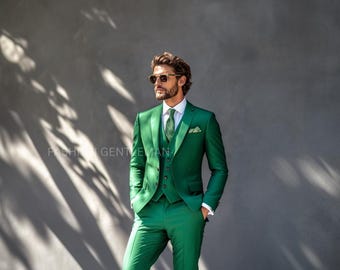 May include: A man wearing a green three-piece suit with a patterned tie. He is wearing sunglasses and has a beard.