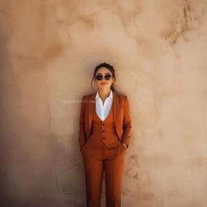 May include: A person wearing a brown suit with a white shirt and sunglasses. The suit includes a vest and a jacket. The person is standing in front of a tan wall.