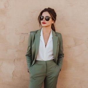 Könnte beinhalten: Eine Frau trägt einen grünen Blazer und eine passende Hose mit einem weißen Hemd mit Kragen darunter. Sie trägt eine Sonnenbrille und hat ihre Haare nach hinten gebunden.