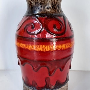 Peut inclure: Un vase décoratif en céramique avec une base et un dessus bruns texturés. Le vase présente un corps rouge vif avec des accents orange et noirs, notamment des motifs tourbillonnants et des rayures horizontales. Le vase a un design artistique unique.