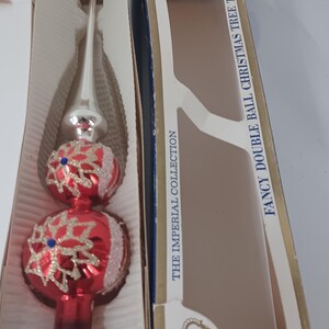 May include: A vintage Christmas tree topper in its original box. The topper is red with white glitter accents and snowflake designs. The box reads "FANCY DOUBLE BALL CHRISTMAS TREE TOP" and "THE IMPERIAL COLLECTION".