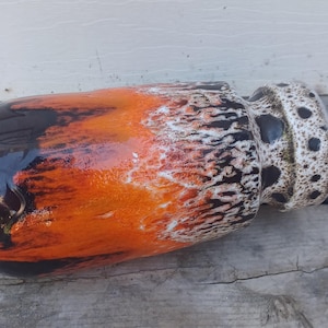 May include: A cylindrical ceramic vase featuring a glossy glaze with a gradient of deep black transitioning into a vibrant orange, accented by a textured white and black speckled pattern around the neck and rim, creating a distinct lava-like effect.