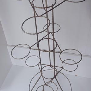 May include: A tall, brown metal plant stand with multiple circular holders of varying sizes. The stand has a three-legged base and a complex, open design, suitable for displaying multiple potted plants. The metal has a slightly textured appearance.