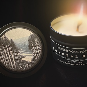 May include: A black candle tin with a white label that reads "Mischievous Potions Coastal Birch" and "natural coconut/soy wax candle". The candle is lit and the wax is melting. The tin has a black lid with a forest scene illustration.