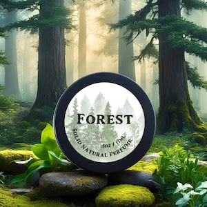 Puede incluir: Una lata redonda negra con una etiqueta blanca que dice "FOREST SOLID NATURAL PERFUME .3 OZ / 15ML". La lata está sentada en una roca cubierta de musgo en un entorno boscoso.