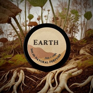 Earth solid natural perfume tin nestled among roots in a forest setting. A deep, earthy, & herbaceous scent with smoky & resinous notes, perfect for nature enthusiasts & those who appreciate a bold, grounding fragrance experience.