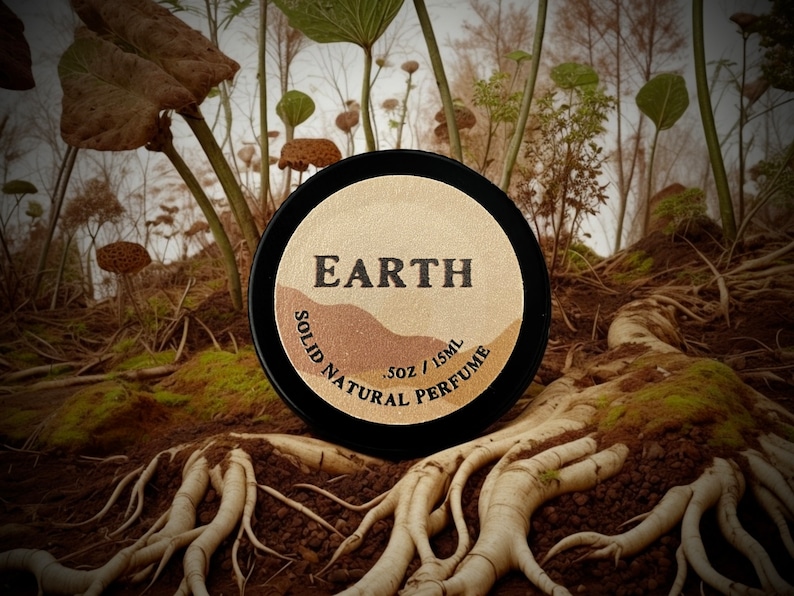 Earth solid natural perfume tin nestled among roots in a forest setting. A deep, earthy, & herbaceous scent with smoky & resinous notes, perfect for nature enthusiasts & those who appreciate a bold, grounding fragrance experience.