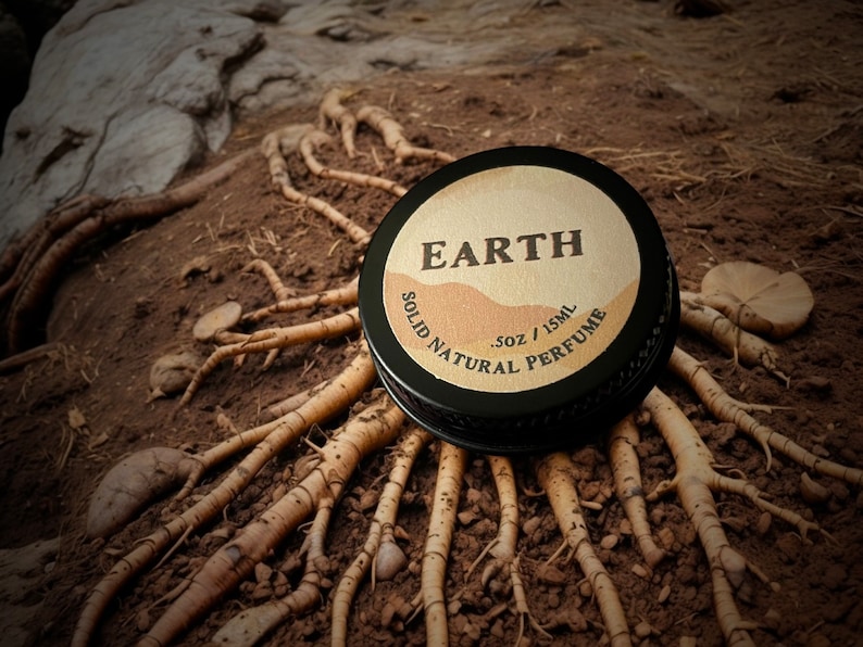 Earth solid natural perfume tin nestled on roots & soil. This earthy fragrance has smoky, woody notes & herbaceous, resinous undertones. Ideal for those seeking a bold, deep & grounding scent inspired by nature. For lovers of natural earthy aromas.