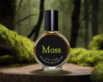 May include: A round glass perfume bottle with a black cap and a black label featuring the green text Moss and the white text .5 oz / 15 ml Extrait de Parfum. The bottle contains a golden liquid and is positioned upright on a wooden surface.