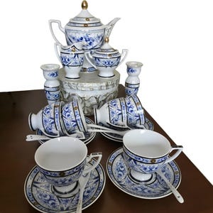 May include: A porcelain tea set featuring a white base with intricate blue floral patterns and gold accents. The set includes a teapot with a lid, a creamer, a sugar bowl with a lid, two candlesticks, four teacups with saucers, and four spoons.