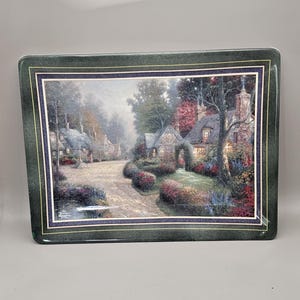 May include: Rectangular serving tray with a scenic village print. The image features a cobblestone road lined with cottages and lush gardens. The tray has a dark green border with a gold accent.