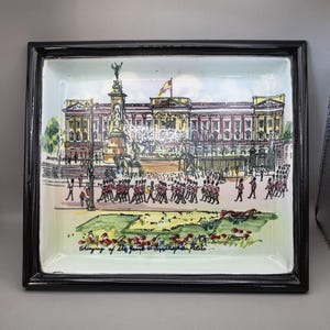 May include: Rectangular ceramic tray with a black frame. The tray features a colorful illustration of Buckingham Palace, with soldiers marching in the foreground. The text "Changing of the Guard at Buckingham Palace" is at the bottom.