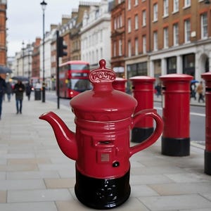 May include: A glossy red ceramic teapot shaped like a traditional British pillar post box. The lid features a crown-like finial with the word POST embossed on it. The base is painted black, and the body includes a molded mail slot and circular details.