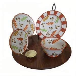 May include: A ceramic dinnerware set featuring two plates and one bowl with a white base, decorated with a pattern of orange, yellow, and green oak leaves and brown acorns. The plates have a textured orange rope-style rim and striped border.