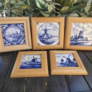 May include: Five framed ceramic tiles with blue and white windmill scenes. The tiles are square and set in light wood frames. The artwork depicts Dutch windmills and landscapes, with a traditional Delftware aesthetic.