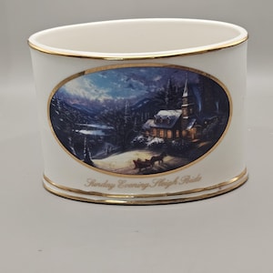 May include: White ceramic decorative holder with gold trim. An oval image depicts a winter scene with a church, horse-drawn sleigh, and the text "Sunday Evening Sleigh Ride".