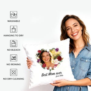 May include: A white square throw pillow featuring a heart-shaped floral wreath surrounding a photograph of a person. Below the heart, the text reads Best Mom ever from Bella. Care icons on the left include Washable, Hanging to dry, No bleach, No ironing, and No dry cleaning.