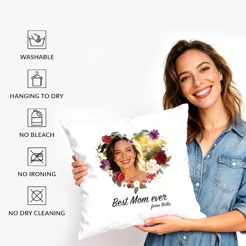 May include: A white square throw pillow featuring a heart-shaped floral wreath surrounding a photograph of a person. Below the heart, the text reads Best Mom ever from Bella. Care icons on the left include Washable, Hanging to dry, No bleach, No ironing, and No dry cleaning.